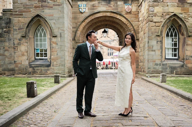 Newly engaged couple walking together through a historic stone archway